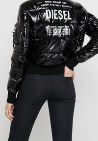 Svart pufferjacka med glänsande yta, ribbade ärmar och tryckt vit text på baksidan. Matchas med svarta åtsittande jeans.