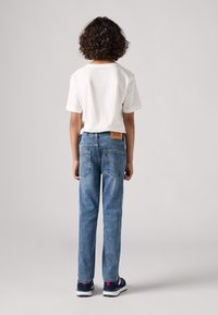 Jeans de mezclilla azul con corte recto y dos bolsillos traseros, combinados con una camiseta blanca de cuello redondo. Tejido texturizado, diseño casual.
