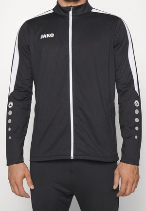 Mand iført en sort JAKO lynlåstrøje med hvide striber på ærmerne og cirkulære logoer på underarmene, vist fra nakke til hofter.