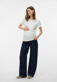 Maternity outfit featuring a white short-sleeve top and loose dark blue denim pants, paired with beige sneakers. Simple design, casual style.