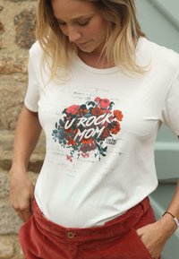 Witte katoenen t-shirt met een kleurrijke bloemrijke grafiek en de tekst "U ROCK MOM." Gecombineerd met rode corduroy broeken, die een ontspannen pasvorm hebben.