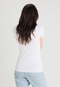 Top blanco de manga corta con un diseño ajustado y textura suave, combinado con unos pantalones vaqueros de denim azul claro. La vista trasera muestra un estilo sencillo.