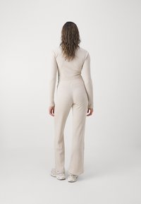 Cremefarvet, ribbet jumpsuit med lange ærmer og flagrende ben. Blød tekstur, tætsiddende design. Bæres med lyse sportssko.