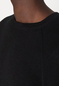 Pull noir en maille avec un col rond, un tissu texturé et des coutures nettes. Remarquable pour sa simplicité et sa polyvalence.