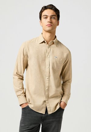 Camicia beige a maniche lunghe realizzata in un tessuto texturizzato, con chiusura a bottoni, colletto e una tasca con patch logo.