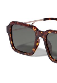 Lunettes de soleil écaille de tortue avec une monture épaisse et angulaire et des verres gris foncé. Des branches en métal fines complètent le style audacieux.