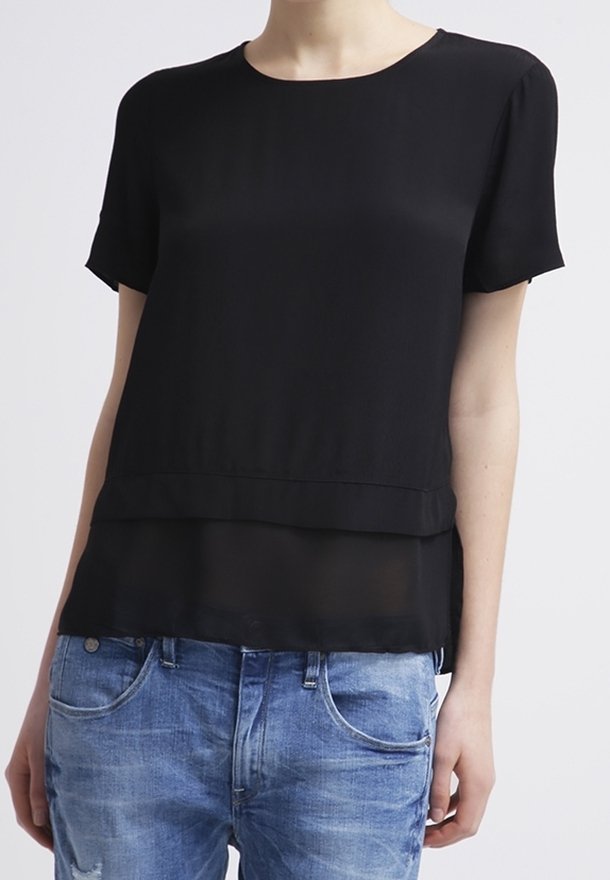 Svart kortärmad blus med lagerdelsprint, tillverkad av lättviktig tyg. Matchad med blå slitna jeans. Slät textur och enkel design.