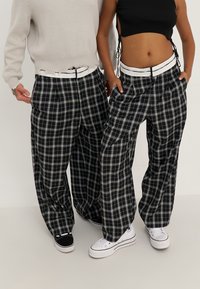 Svart och vit rutig byxor med en bred, lös passform, med en vit midja. Bärs med avslappnade skor; minimalistisk stickad topp.