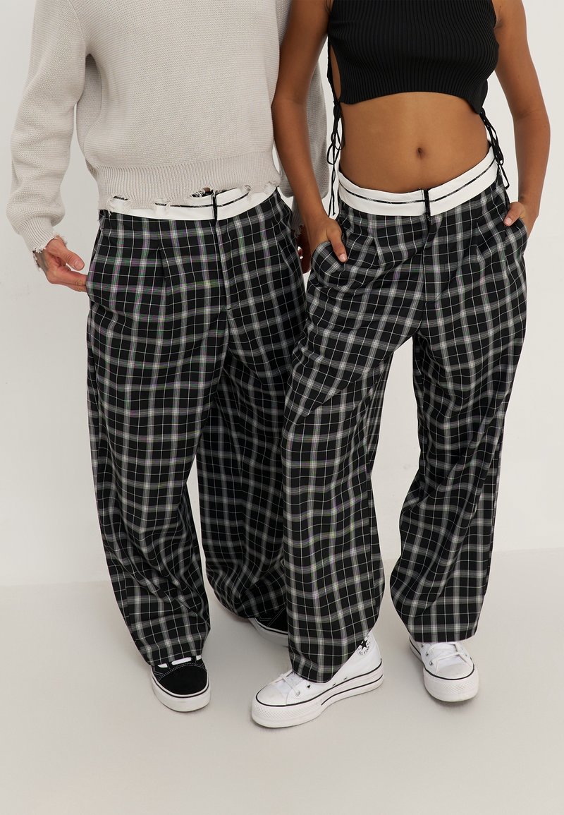 Svart och vit rutig byxor med en bred, lös passform, med en vit midja. Bärs med avslappnade skor; minimalistisk stickad topp.