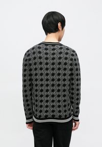 Juodas megztinis su geometriniu pilkų spalvų raštu, su briaunuotu kaklu ir rankogaliais. Dizainas matomas iš nugaros pusės.