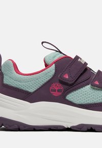 Baskets violet et bleu sarcelle avec des accents roses, tissu en mesh, double brides Velcro, semelle épaisse blanche, et logo arbre Timberland sur le côté.