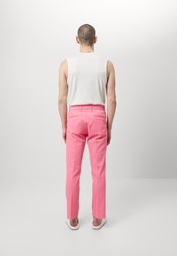 Spodnie z bawełnianej mieszanki w jaskrawym różowym kolorze, z prostą nogawką, dwoma tylnymi kieszeniami i gładkim pasem, zestawione z białą koszulką bez rękawów.