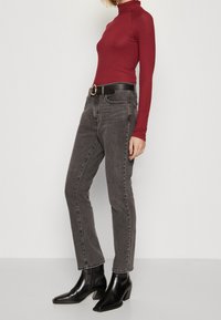 Top de cuello alto ajustado rojo, combinado con pantalones oscuros de talle alto y una cinturilla negra con hebilla dorada. Botines negros completan el atuendo.