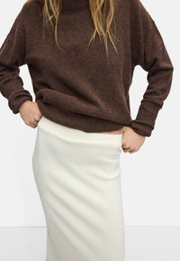 Brązowy, teksturowany sweter z wysokim dekoltem, zestawiony z dopasowaną, kremową, żeberkowaną spódnicą. Całość charakteryzuje się luźnym krojem.