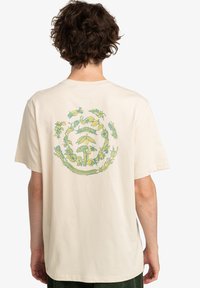 Cream-colored cotton t-shirt featuring a circular, multicolored nature-themed graphic, including plants and animals on the back.