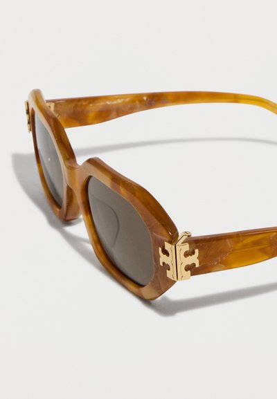 Lunettes de soleil carrées à motif écaille de tortue avec verres foncés et détail décoratif doré sur la charnière des branches.