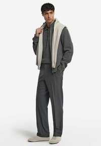 Grauer Strickpullover über einem grauen Poloshirt, kombiniert mit weiten grauen Hosen und hellgrauen Schuhen. Glatte Texturen und geschichtetes Design.