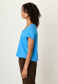 Modra kratka majica s kratkimi rokavi in V-izrezom, izdelana iz lahke tkanine. Ohlapen dizajn, rahlo skrajšana dolžina, z raztrganim robom.