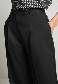 Black tailored trousers made from smooth fabric, featuring a high waist, side pockets, and a structured silhouette with subtle pleats.