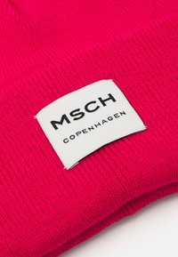 Gorro de punto de color rosa brillante con borde doblado, que presenta una etiqueta rectangular blanca con "MSCH COPENHAGUEN" grabada en texto negro.
