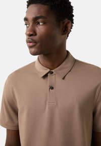 Koszulka polo khaki wykonana z gładkiej tkaniny, z kołnierzem z klapą, dwoma czarnymi guzikami oraz małym haftowanym logo na piersi.