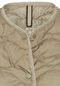 Veste matelassée beige avec col rond, fermeture à boutons-pression, et bord clair le long du col et de l'ouverture frontale.