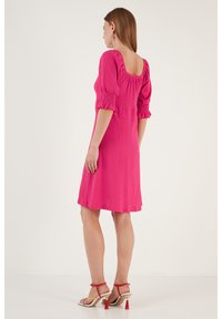 Pink textured dress with short puff sleeves and a square neckline. Above-the-knee length, paired with strappy red heels.