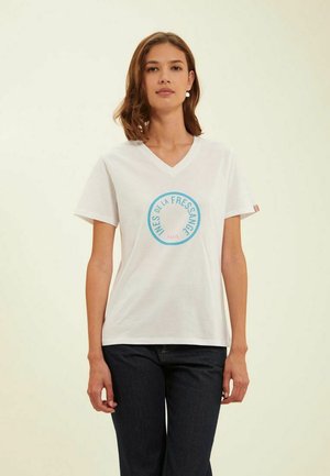 T-shirt en coton blanc avec un col en V et des manches courtes, arborant un logo circulaire bleu avec du texte au centre et des accents rayés sur les manches.