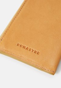Braune Lederbörse mit geprägtem "BONASTRE"-Logo, glatte Oberfläche, abgerundete Ecken und kontrastierende Nähte entlang der Kanten.