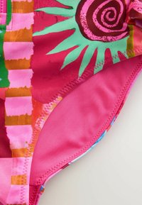 Maillot de bain rose vif avec un motif floral et abstrait coloré. Le tissu a une texture lisse avec des bords cousus.