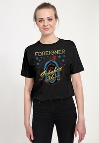 Czarna koszulka z kolorową grafiką jukeboxa i napisem "FOREIGNER". Projekt zawiera gwiazdy i retro estetykę.