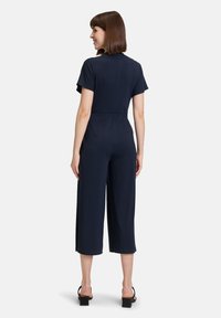 Tuta blu navy realizzata in tessuto liscio, con un corpino aderente, maniche corte, gambe larghe e corte, e un design minimalista.