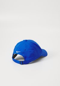 Casquette bleue en tissu léger avec un visière incurvée. Dispose d'une sangle ajustable à l'arrière et d'un logo blanc brodé sur le côté.
