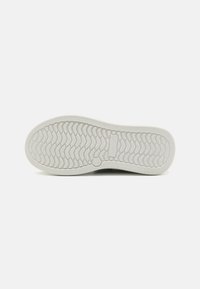 White sneaker sole with a textured tread pattern, featuring a smooth base and raised logo detail near the center.