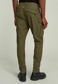 Pantaloni cargo verde oliva con molte tasche, design aderente e tessuto elastico, con un'etichetta logo visibile sulla vita.