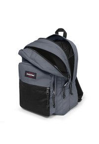 Mochila de tela gris con gran abertura superior, bolsillo frontal de malla negra, dos cierres de cremallera y correas de hombro acolchadas para mayor comodidad.