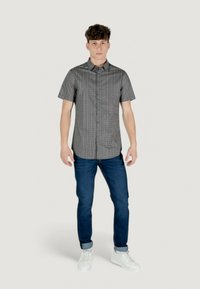 Camicia a maniche corte a righe bianche e nere, abbinata a jeans blu e sneakers bianche, indossata da un modello in piedi.