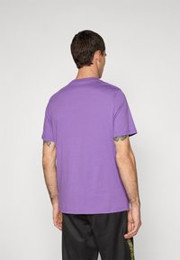 Lilla kortærmet t-shirt lavet af bomuld, med en rund halsudskæring og en afslappet pasform, parret med mørke bukser.