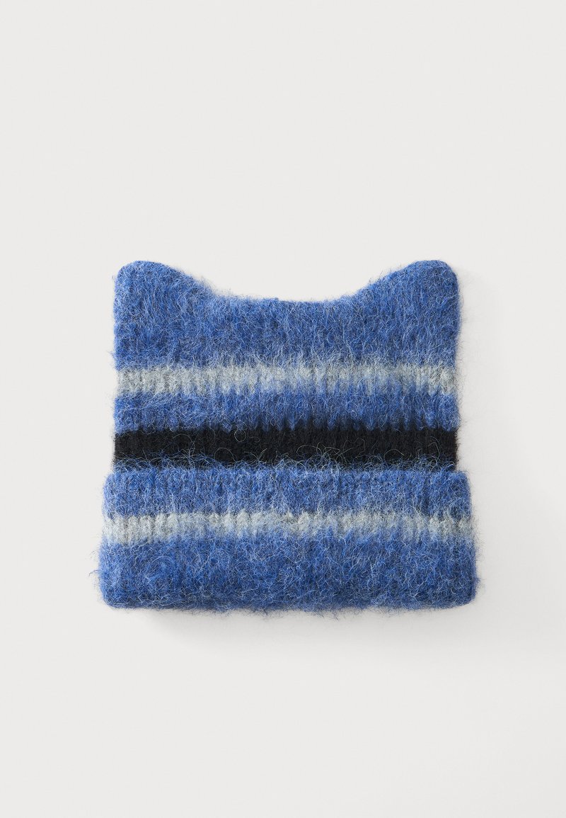 Bonnet tricoté bleu duveteux avec des formes d'oreilles de chat et des rayures horizontales en noir, gris clair et bleu sur fond blanc.