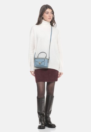 Femme portant un pull à col roulé blanc, une jupe bordeaux, des collants noirs, des bottes montantes noires, et un sac bandoulière bleu clair.
