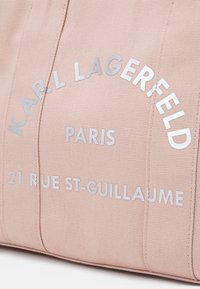 Sac en toile rose avec du texte argenté : "KARL LAGERFELD PARIS 21 RUE ST-GUILLAUME", présentant une surface texturée et un design structuré.