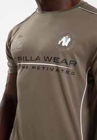 Olijfgroen, vochtafvoerende sportshirt met witte accenten, "GORILLA WEAR" branding en een ronde logo met een gorilla ontwerp.