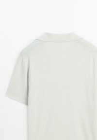 Lys grå kortærmet polo shirt med tekstureret stof og ribbet krave, vist fra ryggen mod en hvid baggrund.