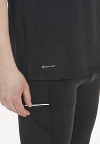 Svart snabbtorkande idrottströja med en slät textur. Har en vit logo på fållen. Tajt passande svarta idrottsbyxor med en liten ficka.