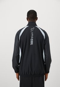 Man wearing a black and gray athletic jacket with "CLIMACOOL" text printed vertically on the back, standing against a plain background.