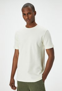 Vit ribbad stickad t-shirt med rund halsringning och korta ärmar, med en slät textur och en avslappnad passform. Matchas med gröna shorts.