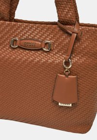 Borsa a rete marrone con due manici robusti; presenta una placca logo in tonalità oro e un'etichetta removibile. Accenti in pelle liscia visibili.