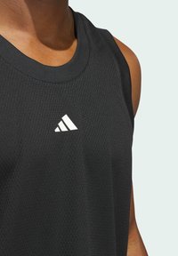 Czarny sportowy top bez rękawów wykonany z teksturowanej tkaniny, z okrągłym dekoltem oraz białym logo Adidasa na piersi.