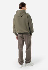 Hanorac verde cu glugă, cu o croială lejeră, purtat cu pantaloni de trening bej deschis. Include manșete cu nervuri, glugă ajustabilă și încălțăminte de stil casual.