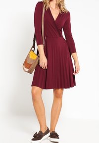 Bordeaux klänning med vikdesign, långa ärmar och plisserad kjol. Matchad med en flerfärgad axelväska och bruna sneakers.